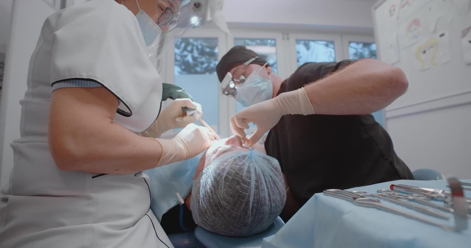 A dentist and an assistant at work over a patient in the chair.