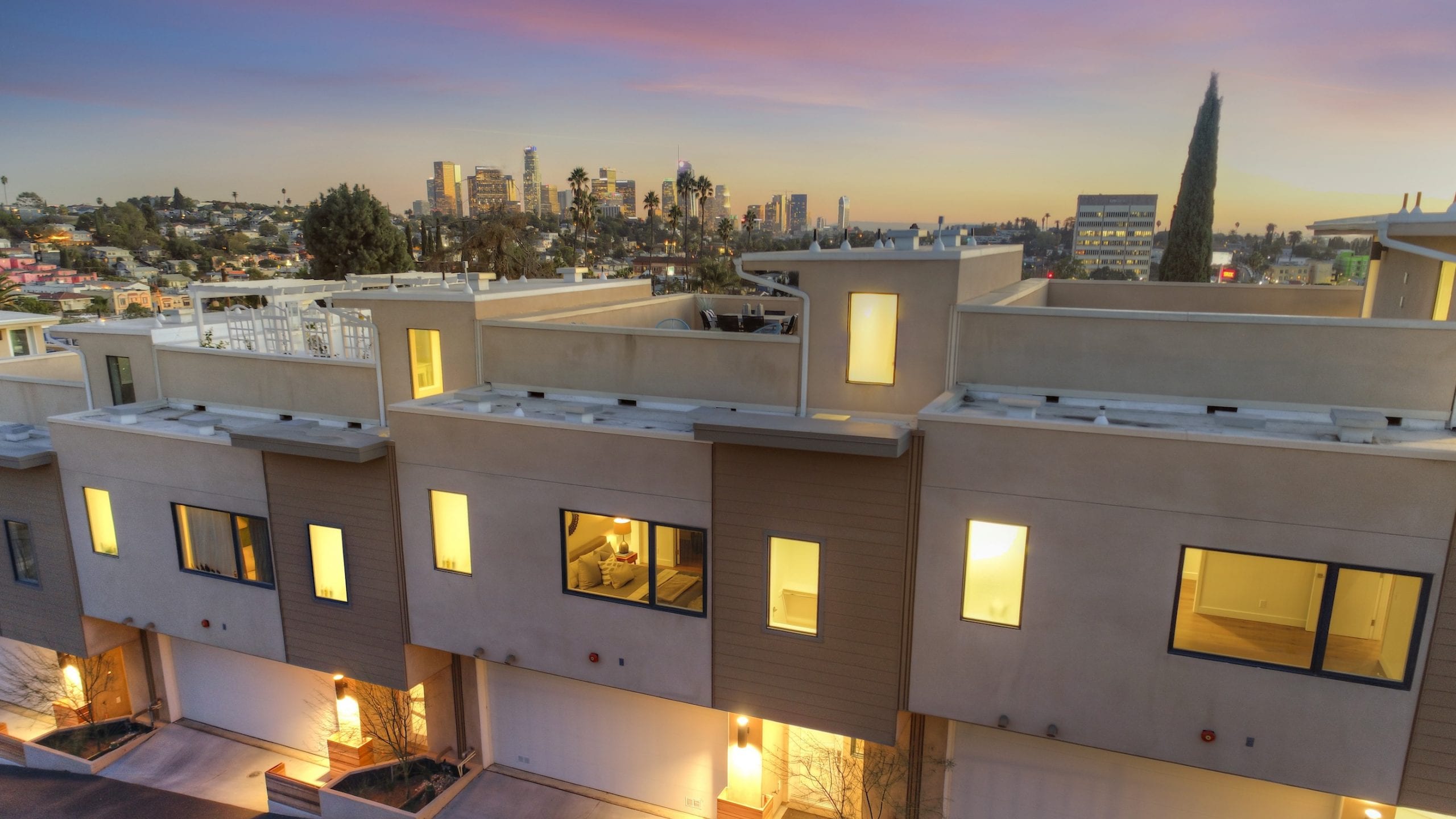 Small-lot homes lit at dusk, with the downtown Los Angeles skyline behind them