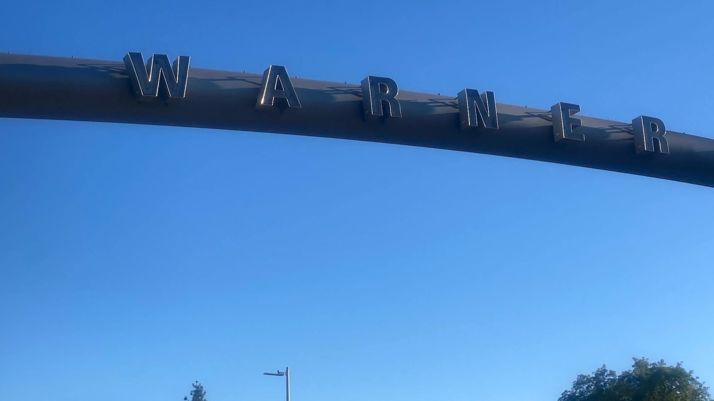 The steel arch over a Warner Center street, its cut-out letters against a blue sky.