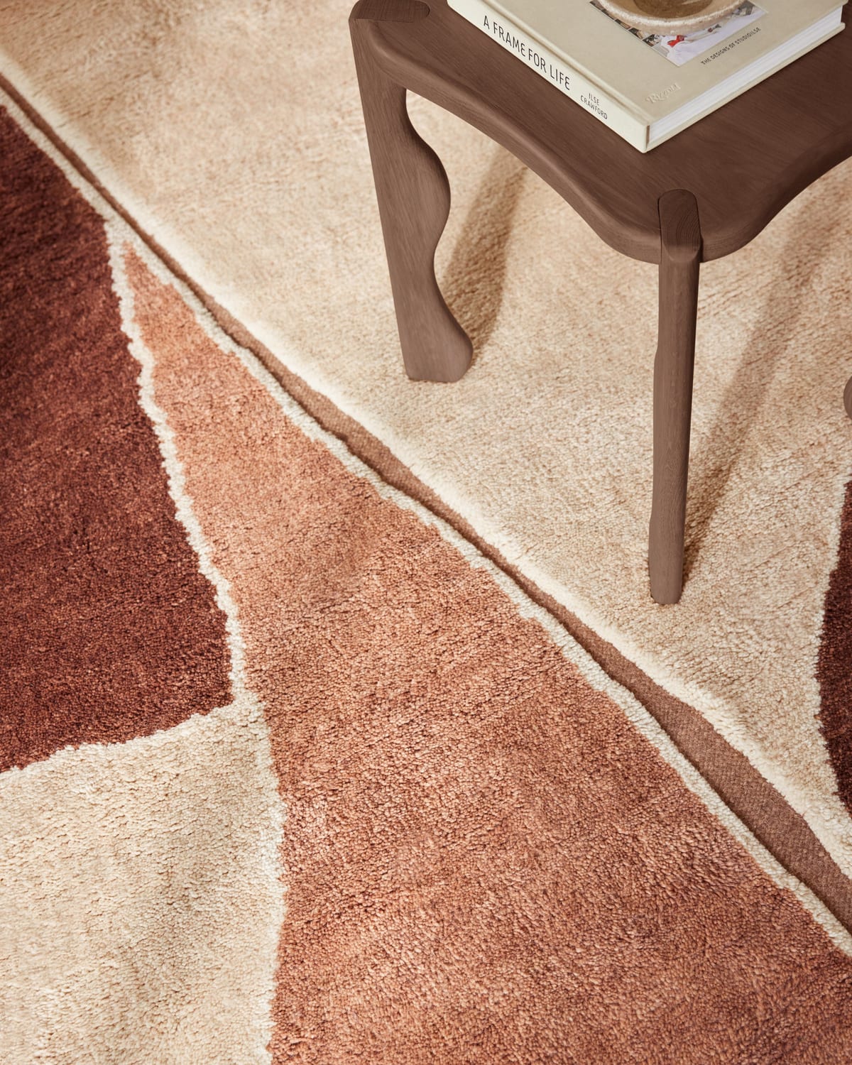 A close view of a flatweave rug in terracotta and cream, a wood table leg on it