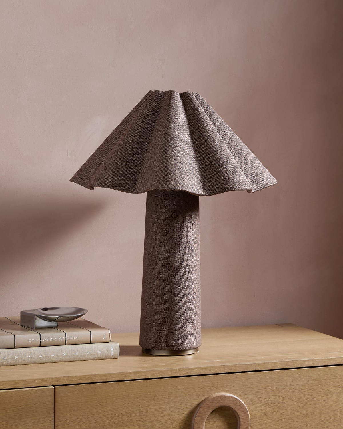 A table lamp with a fluted shade on a light wood sideboard against a mauve wall