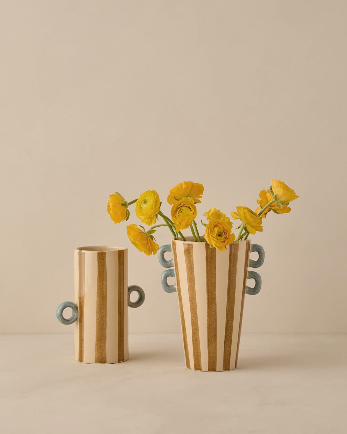 Two hand-painted striped ceramic vases holding yellow ranunculus
