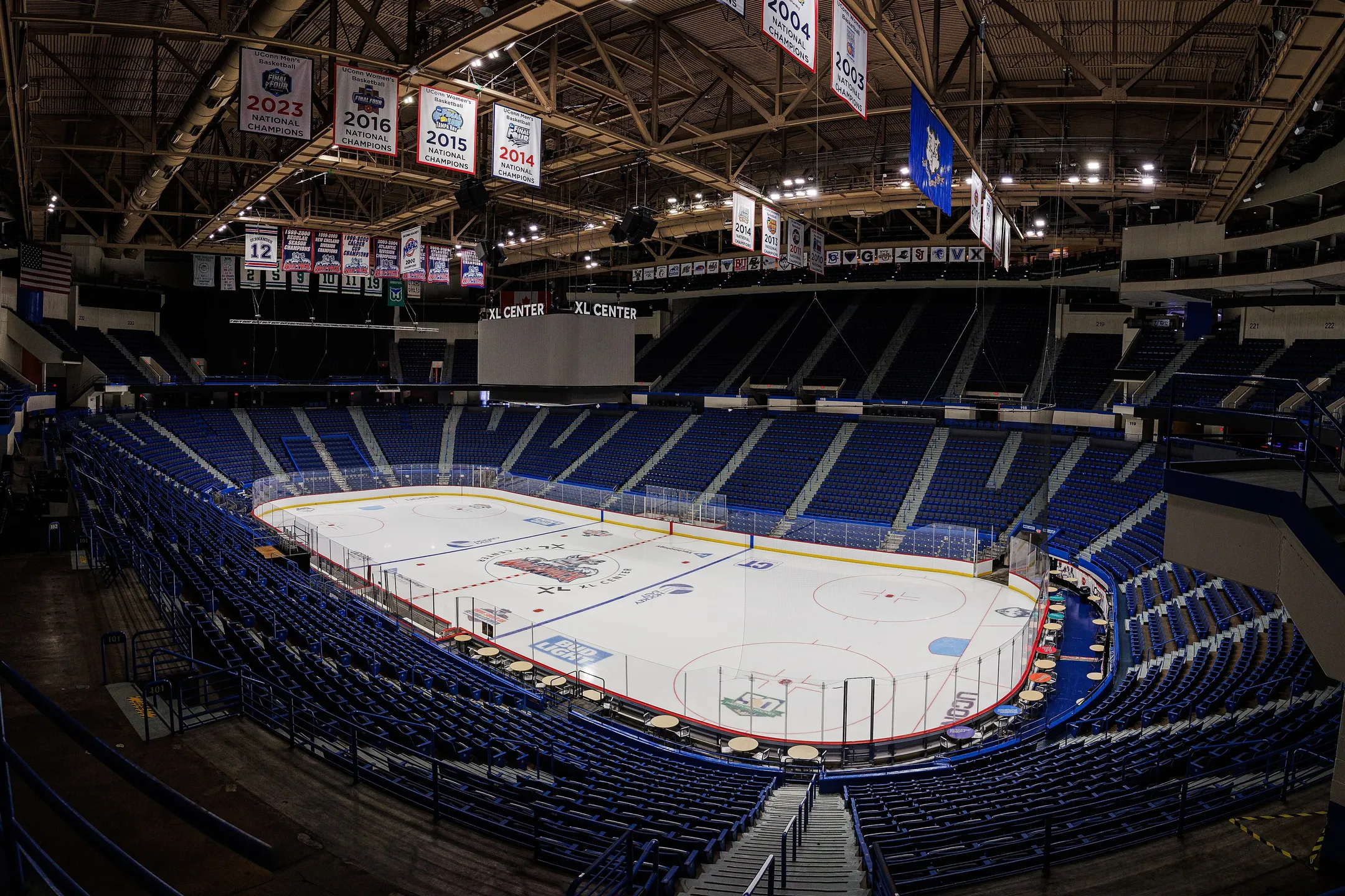 An empty arena bowl from the upper deck: blue seats around the rink, banners in the roof.