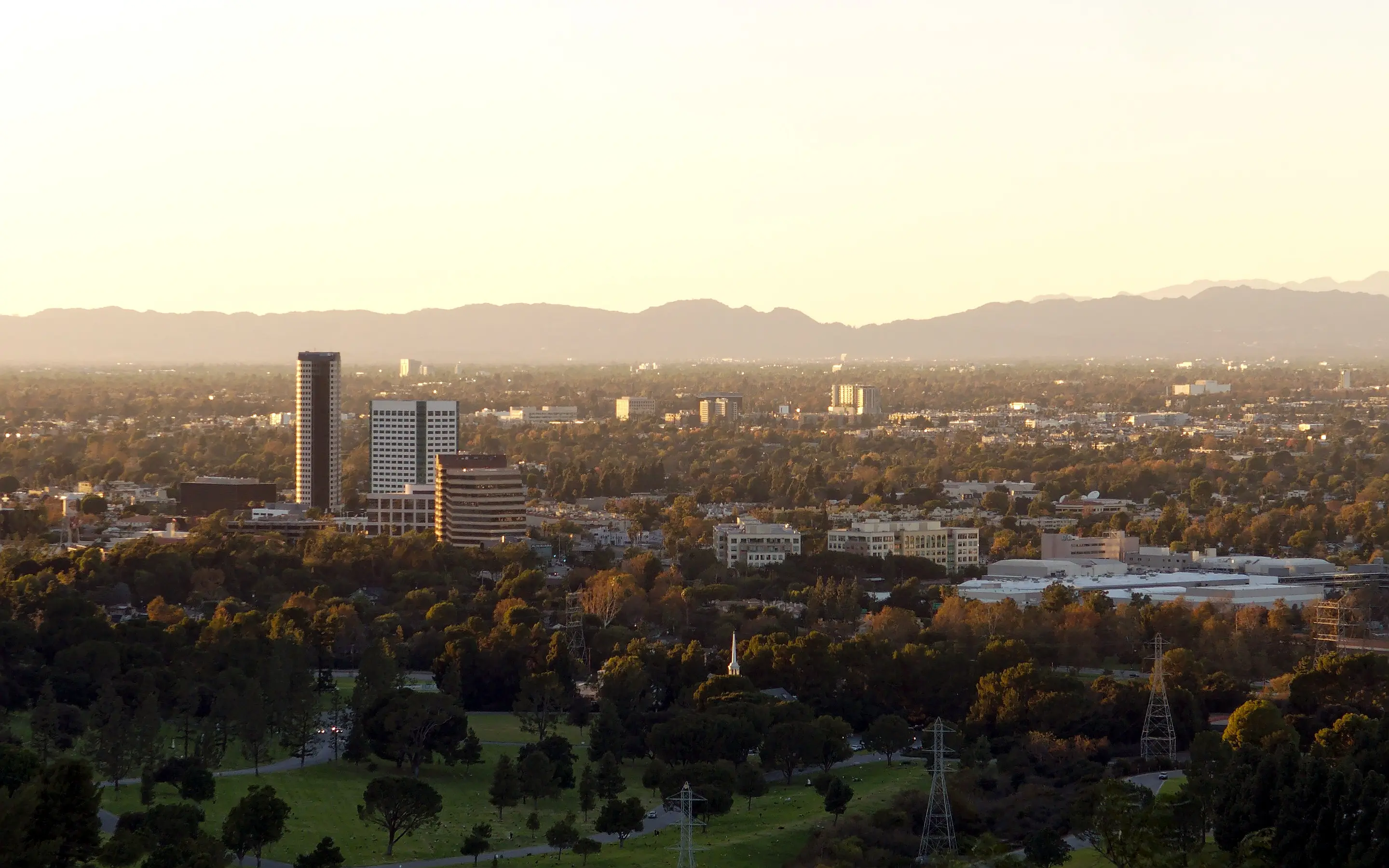 Burbank at golden hour from Griffith Park: office towers over the trees, the San Fernando Valley and the mountains beyond.