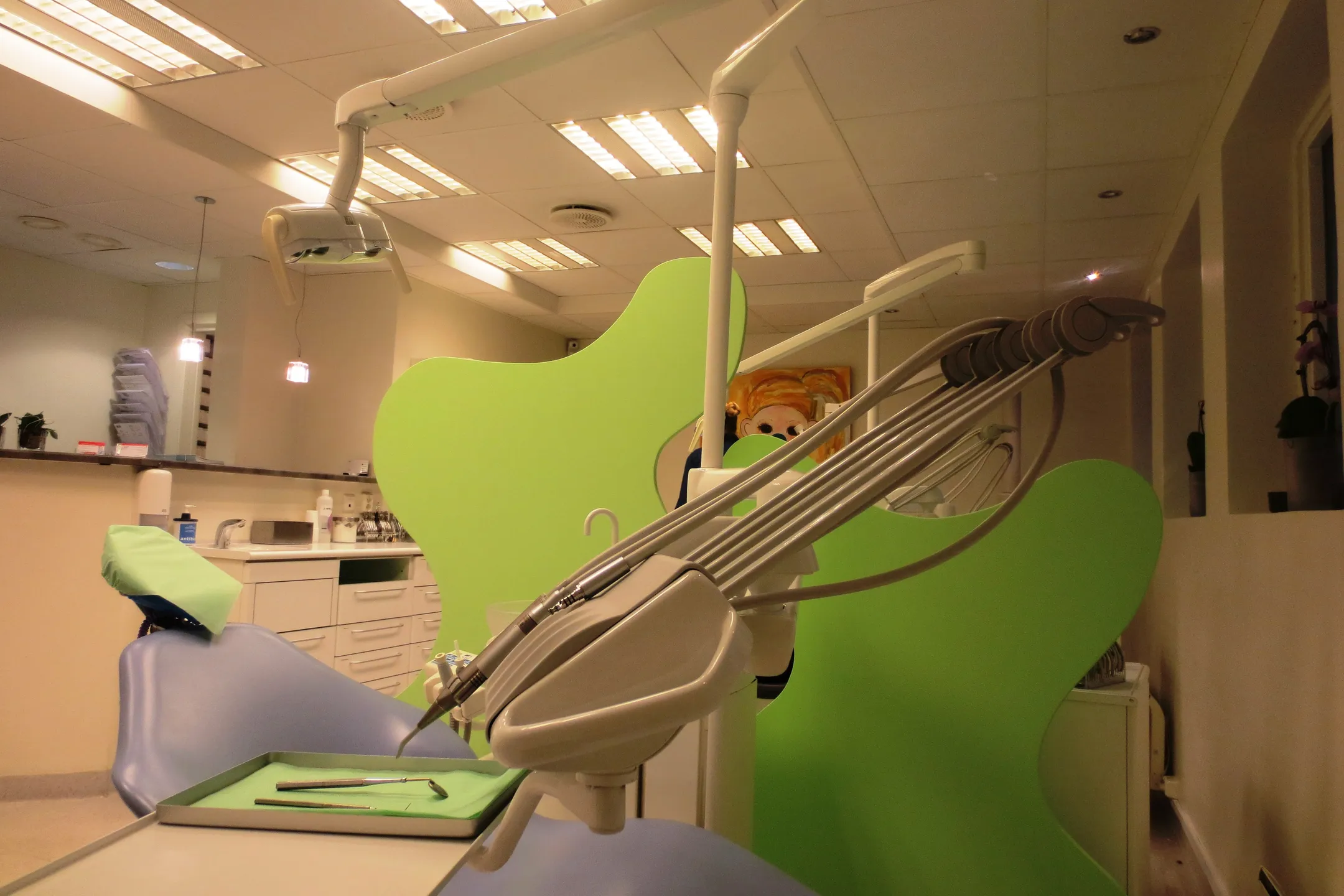 A treatment room: an instrument arm over a lime-green dental chair, a tray of tools beside it.