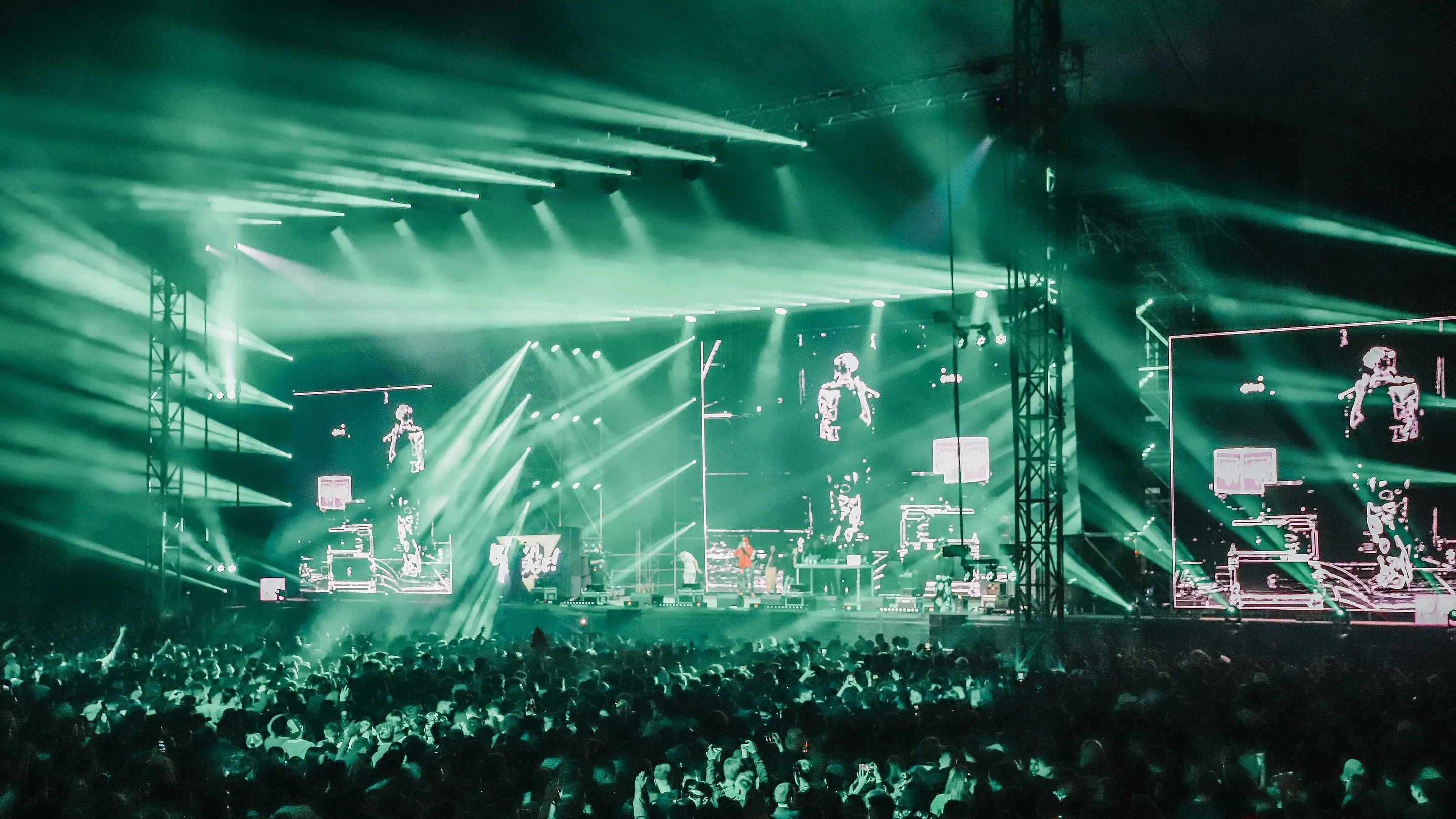 A festival main stage at night: green beams over the rig, the crowd a dark silhouette below.